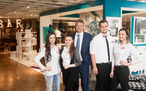 Eine Gruppe von fünf Personen, darunter ein Mann im Anzug, posiert im XXXLutz-Möbelhaus.