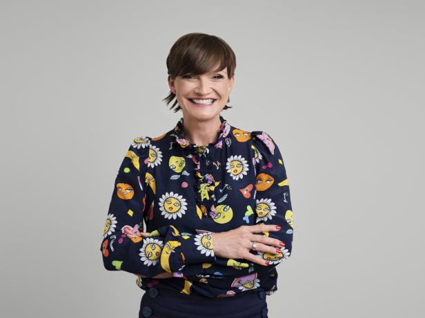 Astrid Steharnig-Staudinger mit verschränkten Armen trägt eine bunte Bluse mit Blumen- und Gesichtermuster.