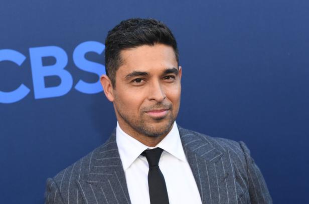 Wilmer Valderrama trägt einen grauen Anzug mit Krawatte vor einem blauen CBS-Hintergrund.