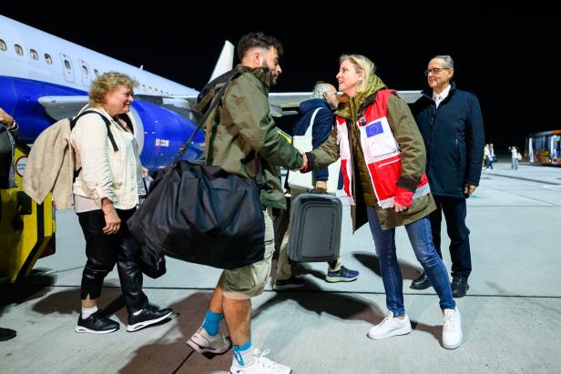 Mehrere Menschen steigen aus einem Flugzeug aus, eine Helferin mit EU-Weste begrüßt einen Passagier per Handschlag.