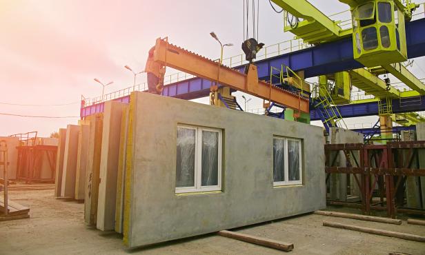A builder installs a concrete floor slab panel at a construction site.