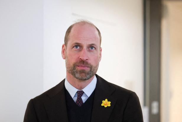 Prinz William mit Bart trägt einen dunklen Anzug, eine gemusterte Krawatte und eine gelbe Narzisse am Revers.