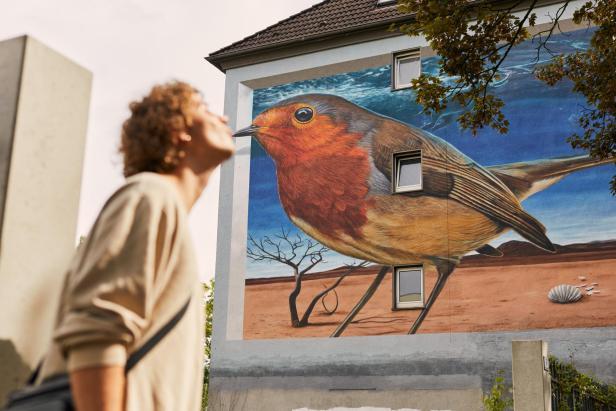 Frau macht Kussmund vor Wandmalerei, wirkt, als würde sie dem gemalten Vogel ein Küsschen geben
