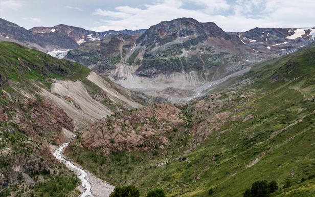 Ein Fluss schlängelt sich durch eine grüne und felsige Berglandschaft.