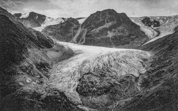 Ein Gletscher erstreckt sich zwischen dunklen Bergen, ein kleiner Bach fließt talwärts.