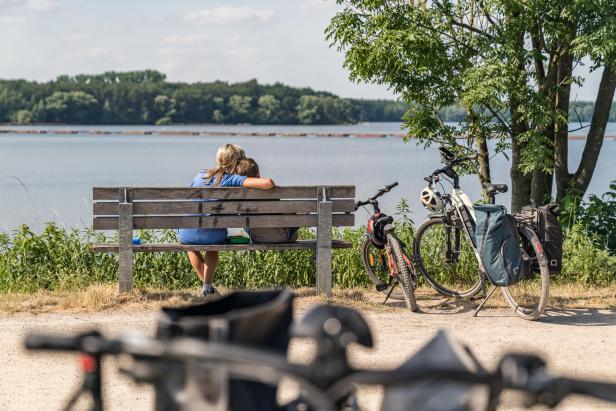 zwei Personen liegen sich auf einer Prkbank im Arm und schauen aufs Wasser