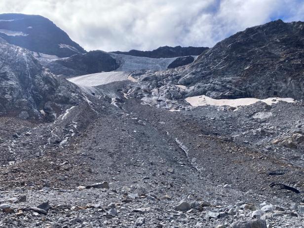 Ein Gletscher erstreckt sich zwischen felsigen Bergen unter einem bewölkten Himmel.