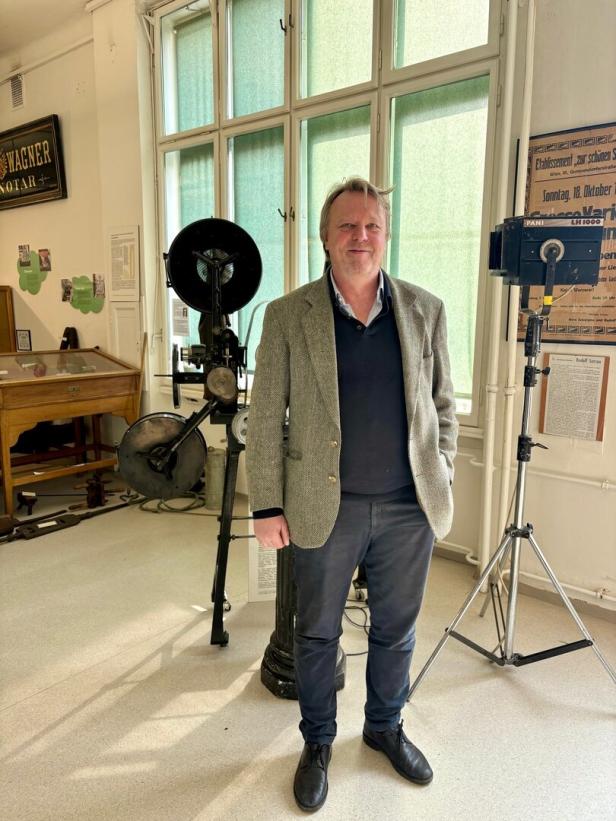 Ein Mann steht in einem Raum mit historischen Ausstellungsstücken und großen Fenstern im Hintergrund.