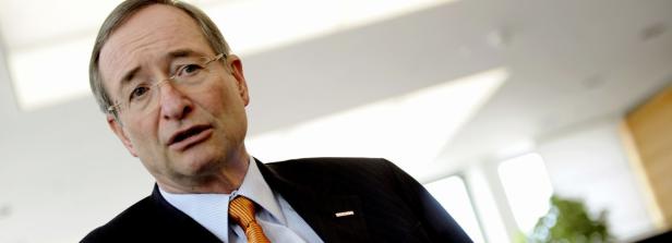 Ein Mann mit Brille, Anzug und orangefarbener Krawatte blickt in die Kamera.