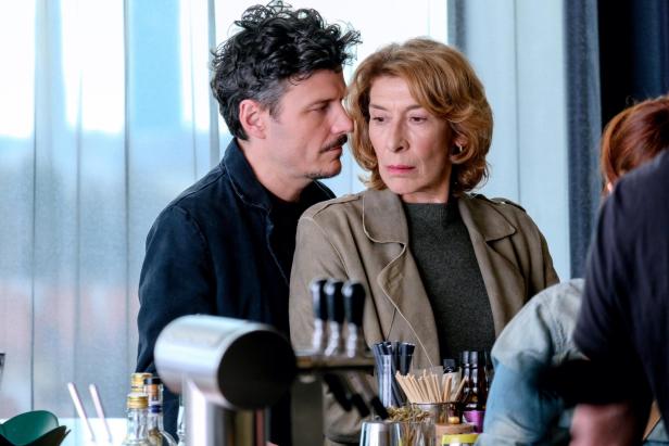 Ein Mann und eine Frau stehen dicht beieinander an einer Theke und blicken ernst zur Seite.