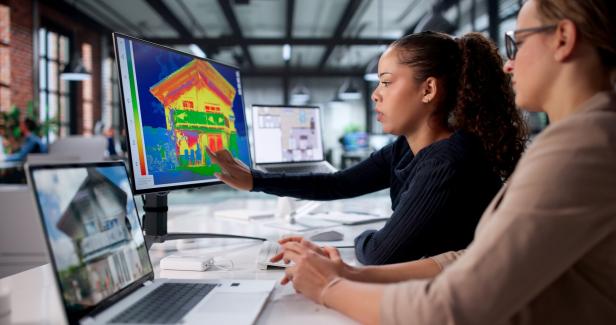 Zwei Frauen analysieren am Computer eine farbige Wärmebildaufnahme eines Hauses in einem modernen Büro.