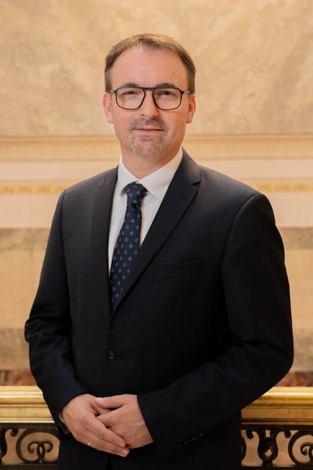 Alexander Pawkowicz steht vor einer marmorierten Wand und blickt freundlich in die Kamera.