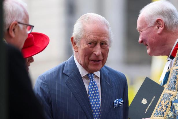 König Charles III. im Gespräch mit einem Mann, der eine Urkunde hält.