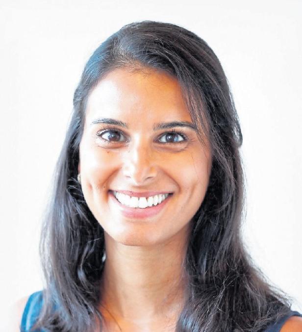 Junge Frau mit langen dunklen Haaren lächelt freundlich und schaut direkt nach vorne vor hellem Hintergrund.