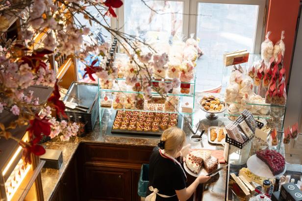 Konditorei mit Kuchen, Gebäck und Süßwaren, eine Frau serviert ein Stück Torte.