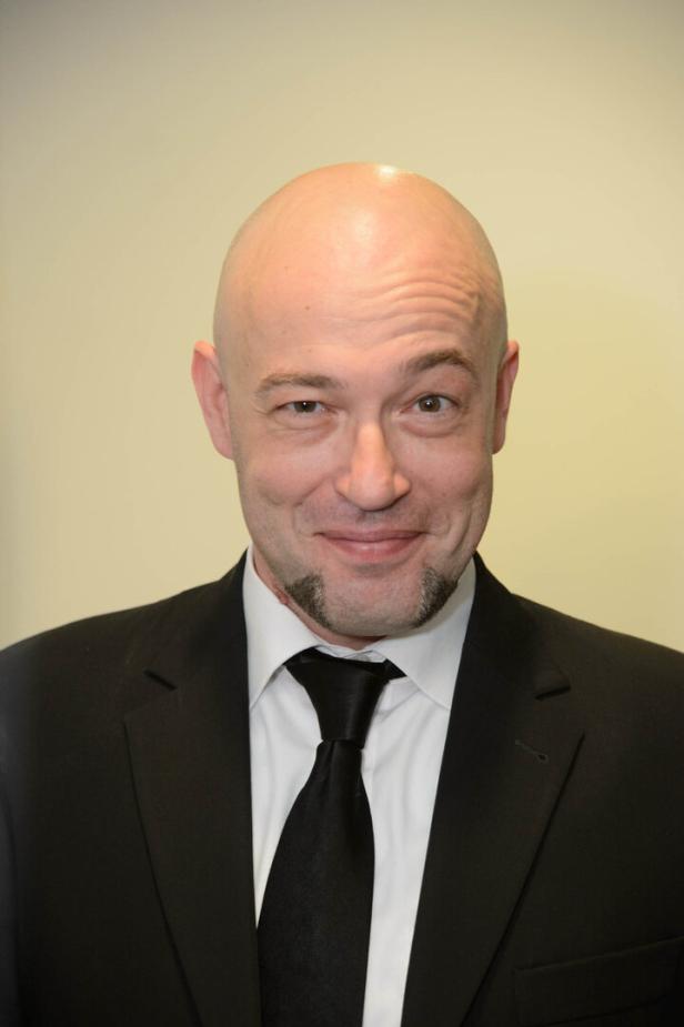 Der Graf mit Kinnbart trägt einen schwarzen Anzug und eine Krawatte.