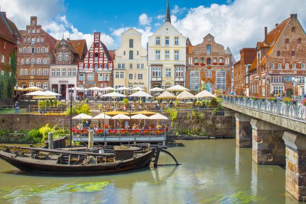 Historische Fachwerkhäuser an einem Fluss mit Straßencafés und Boot bei sonnigem Wetter.