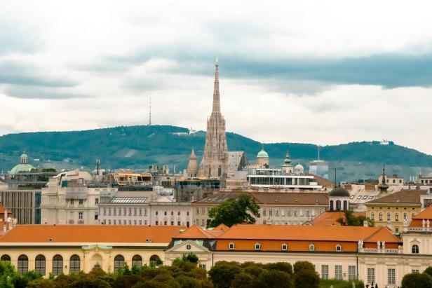 Blick über die Dächer Wiens mit dem Stephansdom im Zentrum und den grünen Hügeln des 19. Bezirks Döbling im Hintergrund.