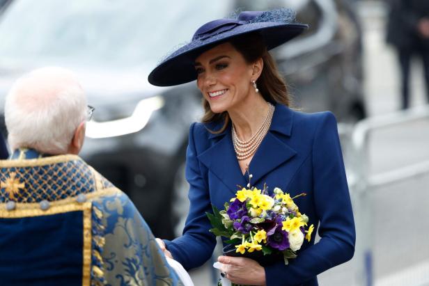 Kate, mit Hut und Blumenstrauß, schüttelt einem Geistlichen die Hand.