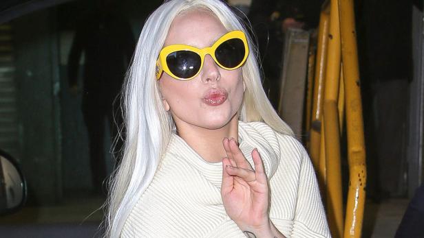 Lady Gaga mit blonden Haaren und gelber Sonnenbrille wirft einen Kuss in die Kamera.