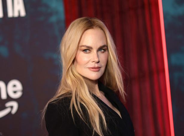 Nicole Kidman mit blonden Haaren und dunklem Blazer vor einem roten Vorhang.