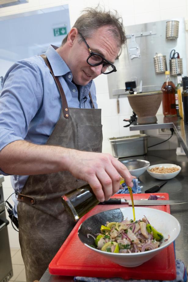 Ein Mann mit Schürze gießt Öl über einen frischen Salat in einer Schüssel in einer modernen Küche.