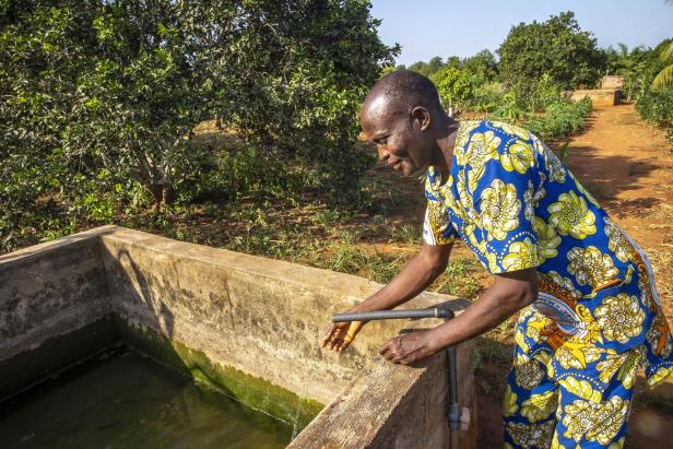 Mann entnimmt Wasser aus einem Betonbecken auf einem grünen landwirtschaftlichen Feld.