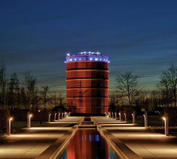 Der Gasometer Oberhausen bei Nacht, beleuchtet und von Bäumen umgeben.