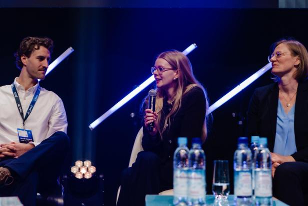 Podiumsdiskussion mit mehreren Personen, ein Frau spricht ins Mikrofon.