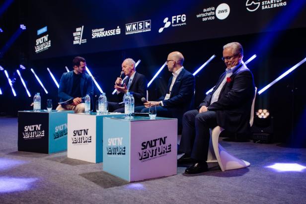 Podiumsdiskussion mit mehreren Personen, ein Mann spricht ins Mikrofon.