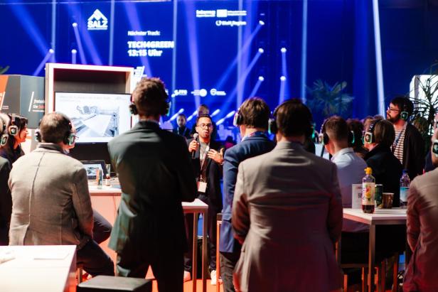 Teilnehmende mit Kopfhörern verfolgen beim SALZ-Festival im Messezentrum Salzburg eine Präsentation zu technologischen Innovationen.