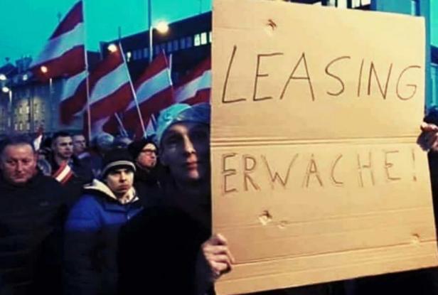 Eine Menschenmenge mit Österreich-Flaggen, eine Person hält ein Schild mit der Aufschrift "LEASING ERWACHE!".