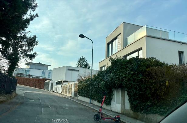 Moderne Wohnhäuser an einer ruhigen Straße mit einem roten E-Scooter auf dem Gehweg und viel Grün an den Hausfassaden.