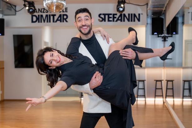 Ein tanzendes Paar posiert lachend in einer modernen Tanzschule mit Holzfußboden.