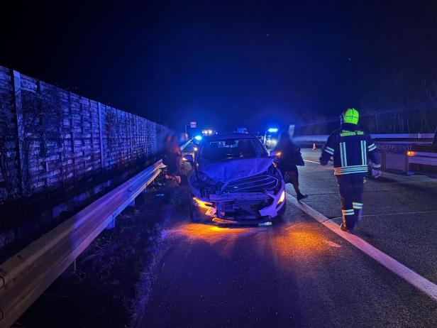 Ein demoliertes Auto nachts auf der äußersten Autobahnspur, ein Feuerwehrmann geht daran vorbei.