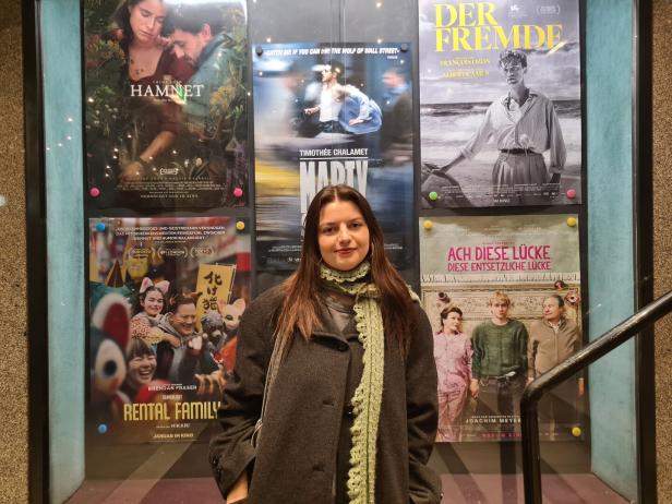 Laura steht vor einer Wand, auf der mehrere Filmposter angebracht sind.