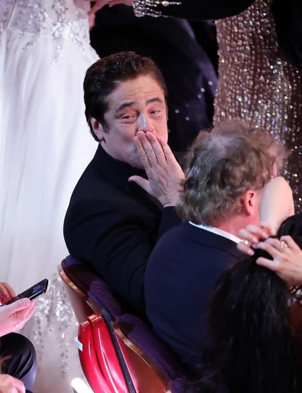 Benicio del Toro in einem schwarzen Anzug schickt einen Kuss in die Menge.