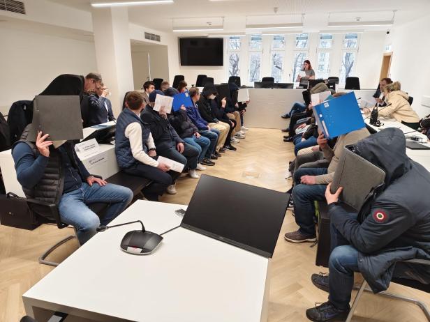 Angeklage halten sich Aktenordner vors Gesicht.