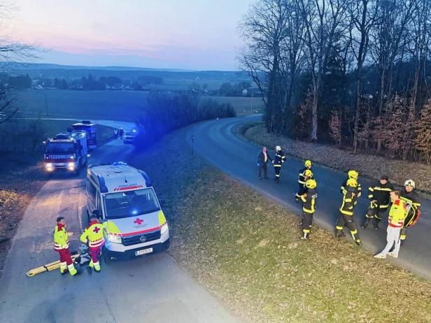 Mehrere Feuerwehrleute und Rettungskräfte stehen an einer Landstraße neben Einsatzfahrzeugen im Abendlicht.