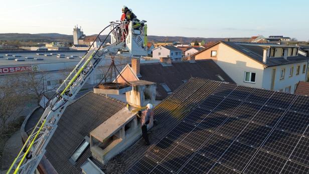 Zwei Arbeiter entfernen mit einer Hebebühne einen Schornstein von einem Dach mit Solarpaneelen.