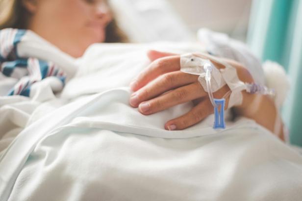 Hand einer Patientin mit Infusionsnadel auf einer Krankenhausdecke.