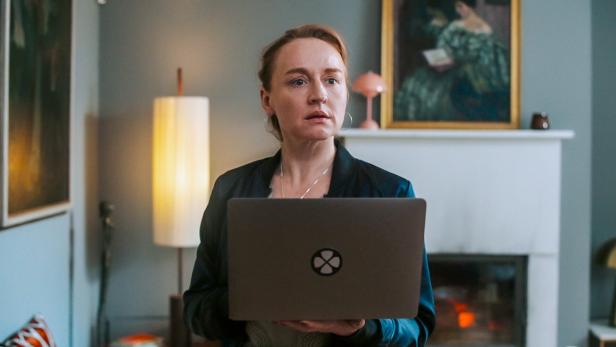 Brigitte Hobmeier hält einen Laptop vor sich, im Hintergrund ein Kamin und ein Gemälde.