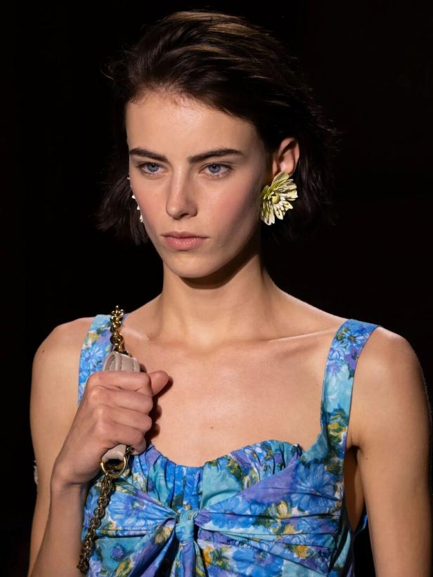 Frau mit blauem Kleid und goldenen Blumen-Ohrringen