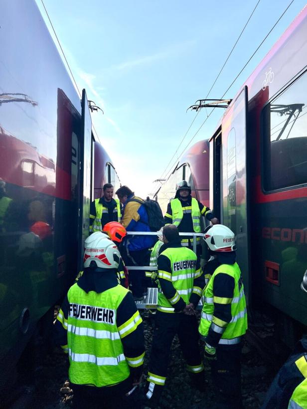 Mehrere Feuerwehrleute helfen zwischen zwei stehenden Zügen bei einer Evakuierungsaktion.