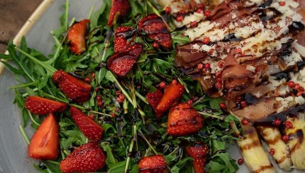 Rucolasalat mit frischen Erdbeeren, gegrilltem Käse und Schinken, garniert mit Balsamico.