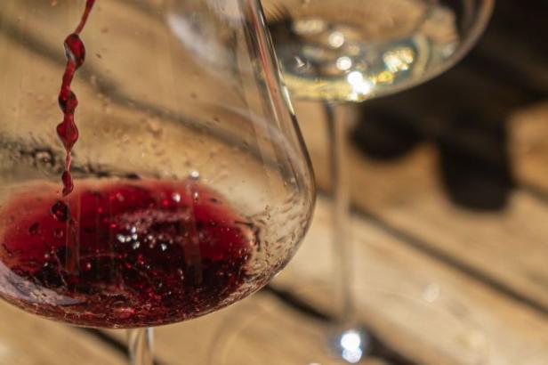 Rotwein wird in ein Glas eingeschenkt, daneben steht ein Glas mit Weißwein auf Holztisch.