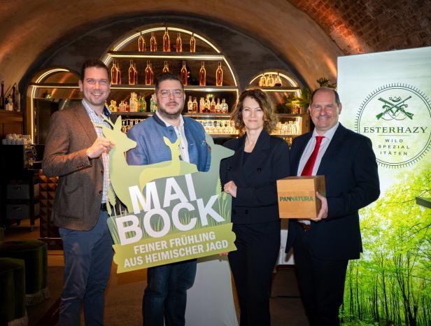 Vier Personen stehen in einem Gewölbekeller, zwei halten ein Schild mit der Aufschrift „MAIBOCK“, eine Person hält eine Holzkiste.