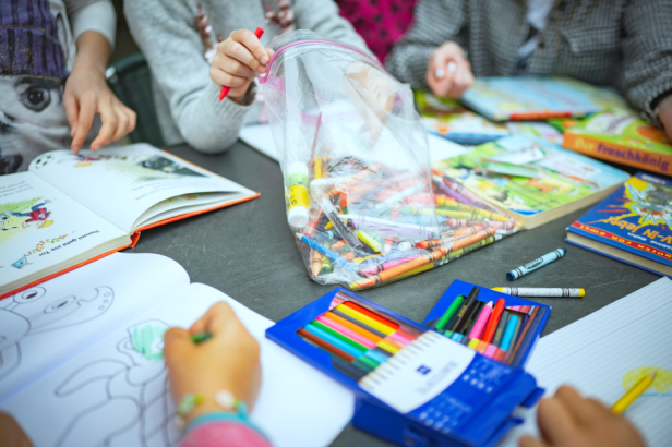 Kinder malen und lesen gemeinsam an einem Tisch mit vielen Buntstiften und Büchern.