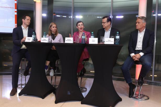 Fünf Personen diskutieren an einem Podium mit Namensschildern und Wasserflaschen.
