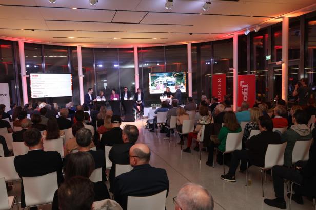 Podiumsdiskussion mit Publikum in einem modernen, hell erleuchteten Veranstaltungsraum.